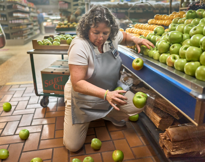 An employee dropping apples at a grocery store.