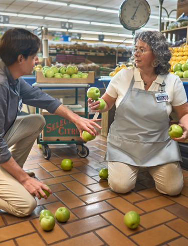 Understanding tardive dyskinesia hero image with a woman picking up apples in a grocery store.